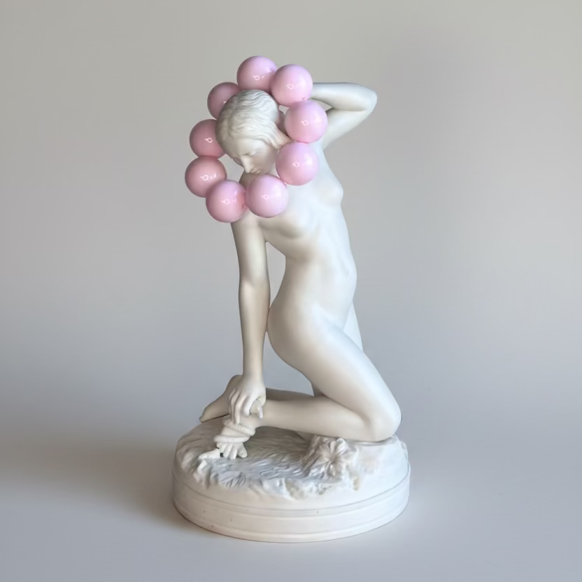 Statue of a nude figure with pink balloons against a textured wall.